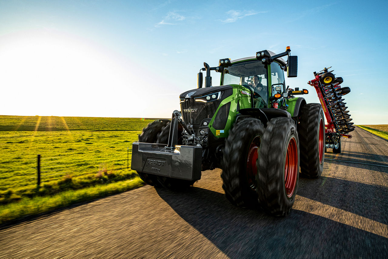 Fendt high-horsepower tractor pulling sunflower tillage equipment down dirt road.