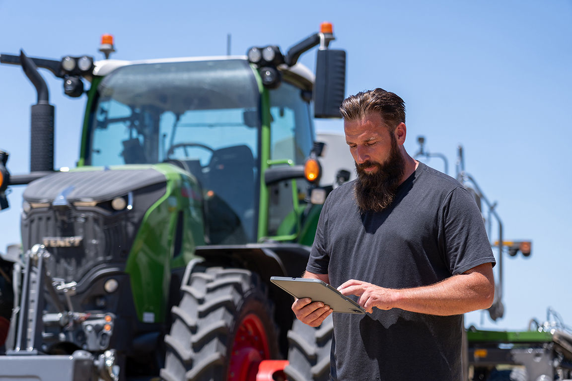 Farmer using a tablet beside a Fendt tractor in the field.