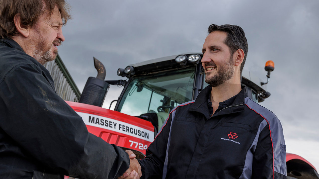 Close up of older man shaking hands with man in MF workwear with MF 7724 tractor visible behind