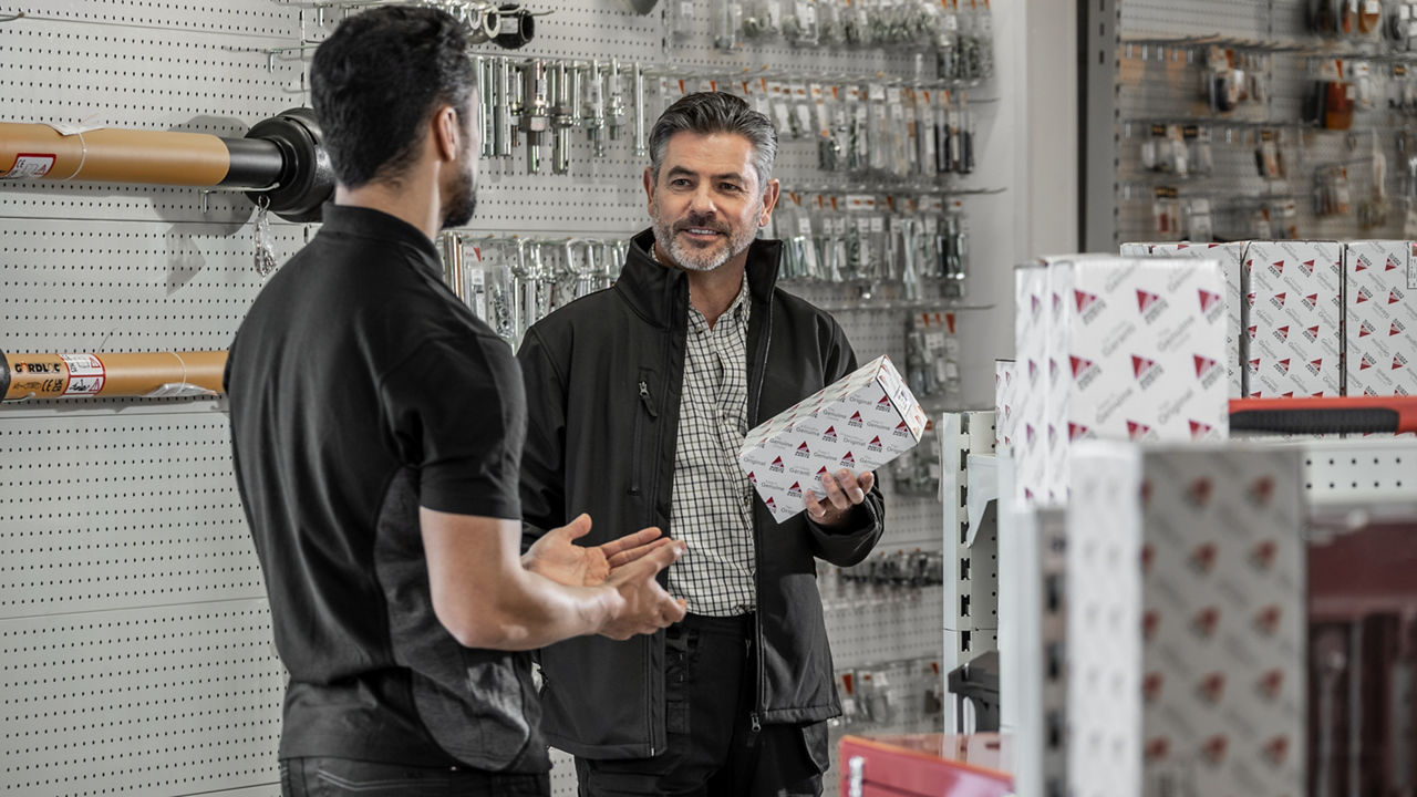 A farmer holding an AGCO Parts box, discussing something with an employee at a dealer