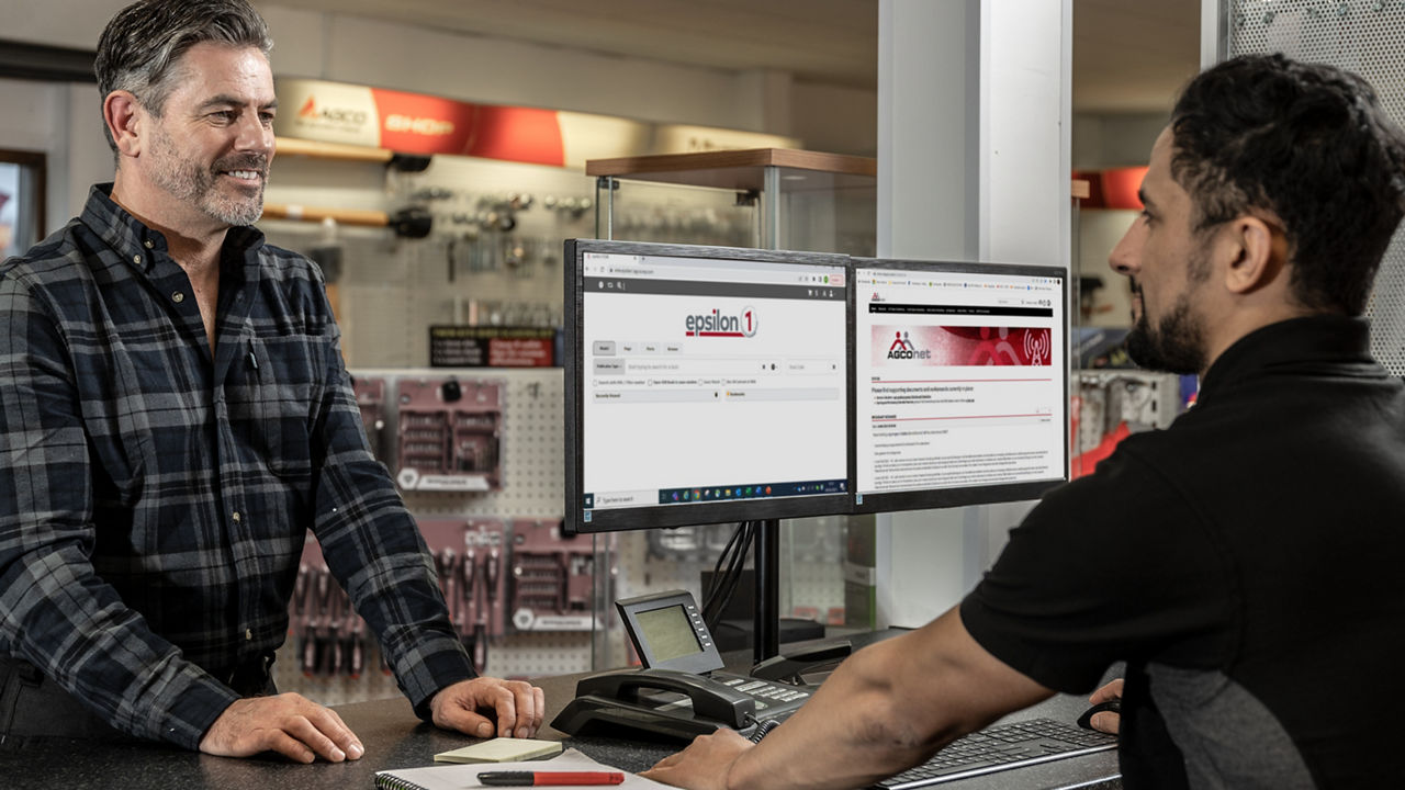 A farmer discussing parts with an employee at a dealer. There are two screens visible with AGCO websites showing