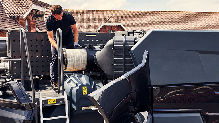 A man replacing a part on top of a combine harvester