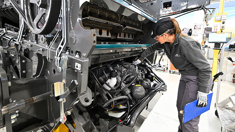 A female technician examining a combine harvester engine