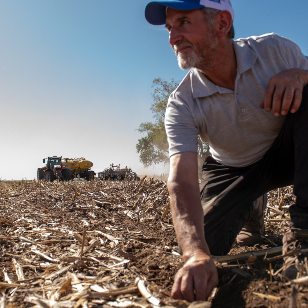 A farmer checks his crop with his tractor in the background