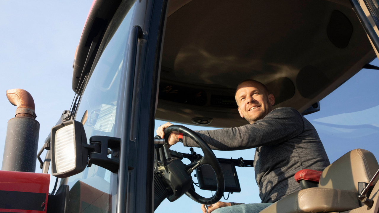 A man smiles from the cab of his tractor.