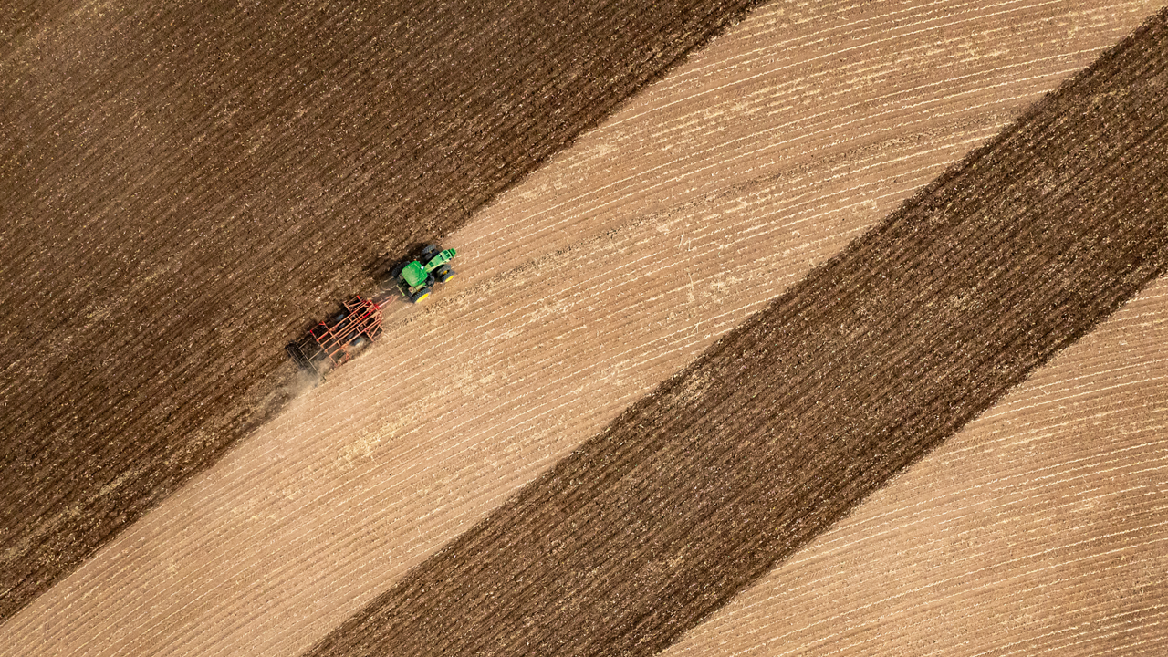 A drone shot of a tractor working a field in straight lines.