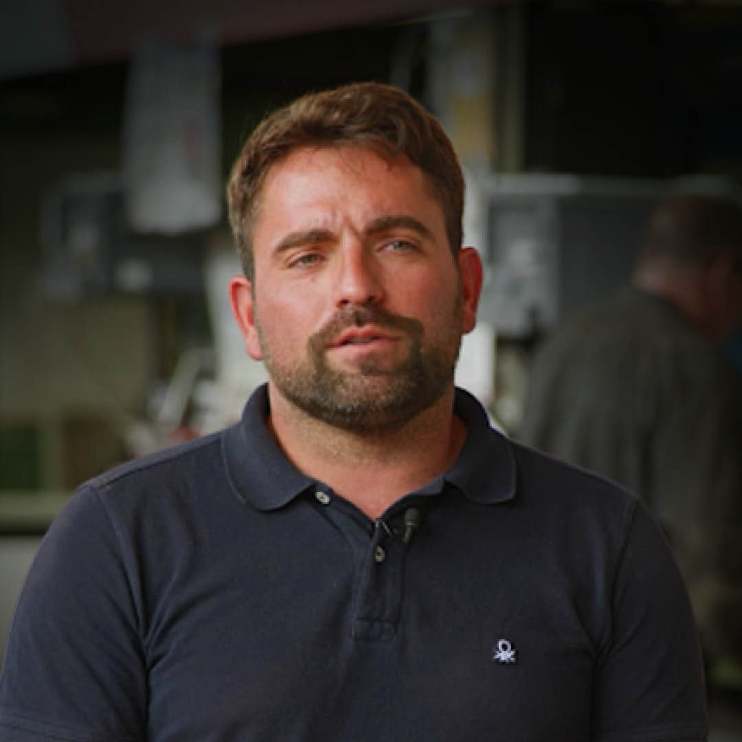 A headshot of Luis Maqueda with a workshop in the background