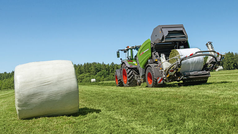 A picture of a Fendt baler on a field with a wrapped bale of hay