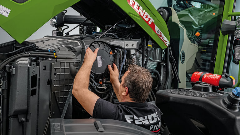 A Fendt technican checking a part underneath a Fendt tractor bonnet