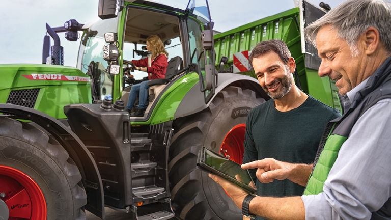 A farmer and a technican looking at an iPad with a tractor in the background