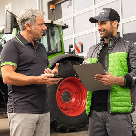 A farmer discussing something with a technican holding a clipboard
