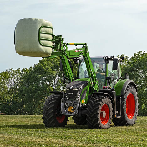 A Fendt tractor with a front loader carrying a bale of hay