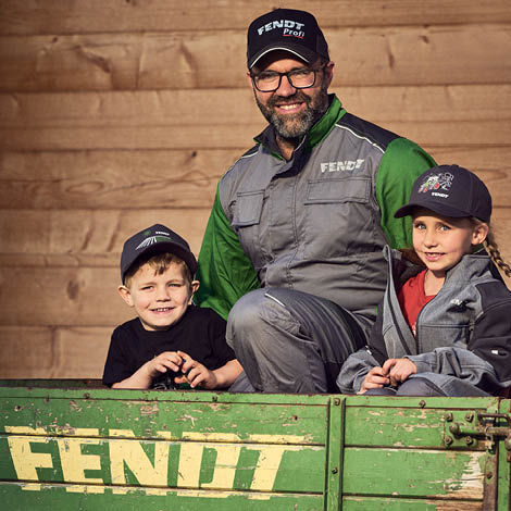 A man and two boys wearing Fendt caps and workwear standing behind a Fendt sign
