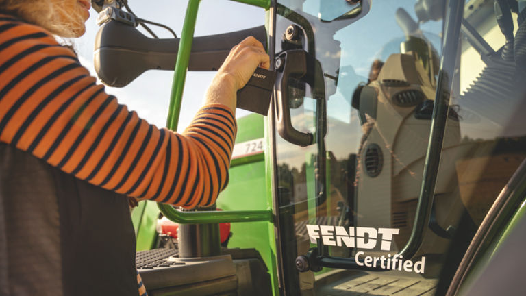 Femme tenant la porte d’un tracteur sur laquelle est inscrit Fendt Certified