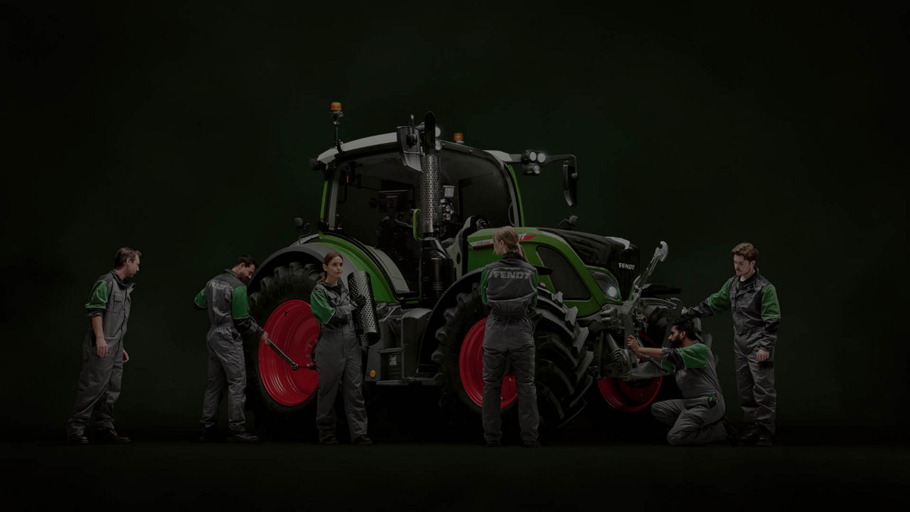 A dark image of a Fendt tractor being worked on by various people