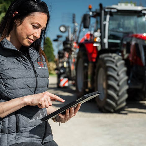 A woman looking at a clipboard with a Massey Ferguson tractor in the background