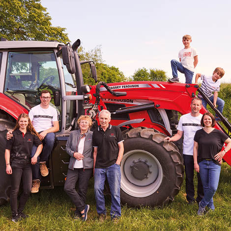 A group of people wearing various items of Massey Ferguson merchandise grouped around a tractor