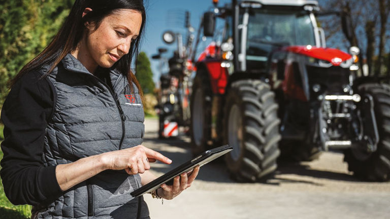 A female technician examining a clipboard with a tractor in the background