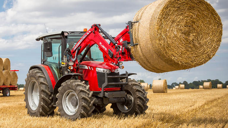 An MF tractor with a front loader holding up a hay bale