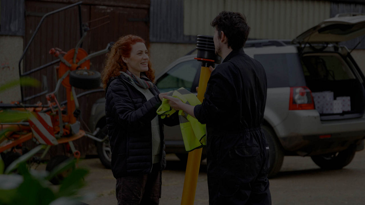 A woman handing a hi vis to a farm labourer