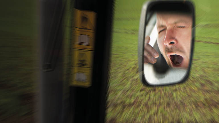 A farmer yawning in a rear view mirror