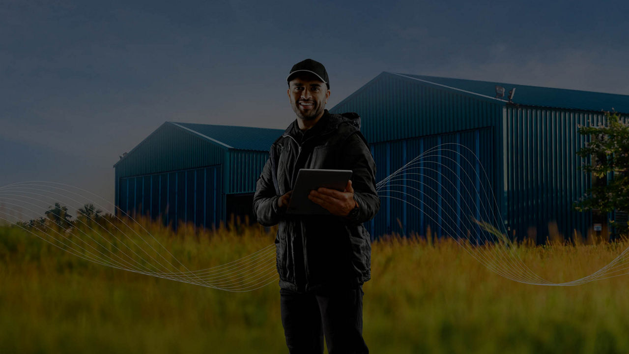 A dark image of a farmer standing in a field smiling while holding an iPad