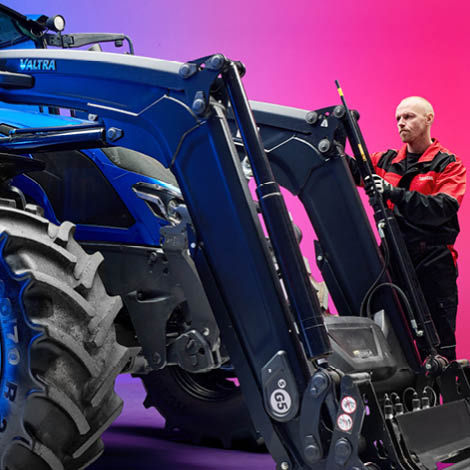 A technician in Valtra workwear examining a front loader on a tractor