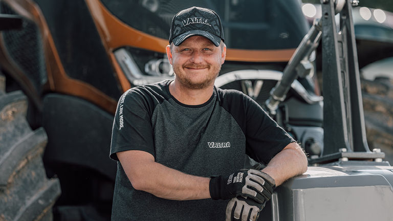 A smiling technican standing in front of a tractor