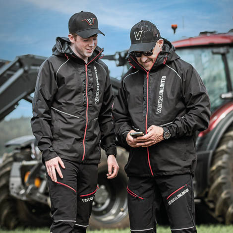 Two farmers wearing Valtra caps and workwear standing and looking at a mobile phone