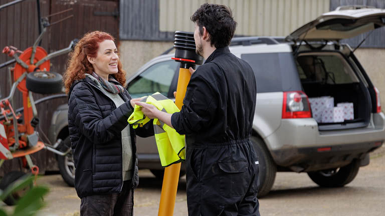 A woman handing a hi viz jacket and PTO tool to a man
