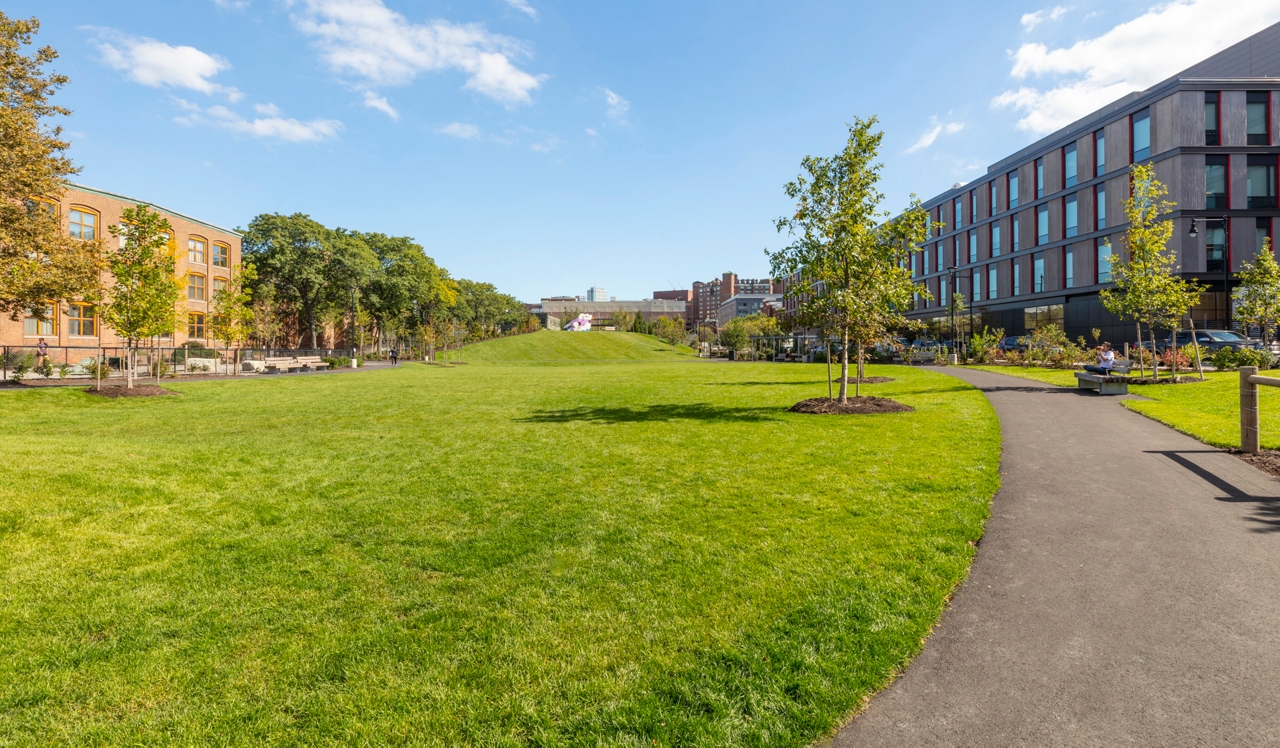 Axiom Apartment Homes - Cambridge, MA - Man sitting on park bench.<div style="text-align: center;">Toomey Park, located one block down the street boasts an off-leash dog park, walking trails, event areas, playgrounds, and even a sledding hill.</div>
