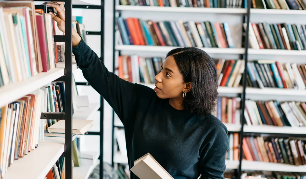 The Left Bank | Philadelphia, PA | Young woman taking book off library shelf 