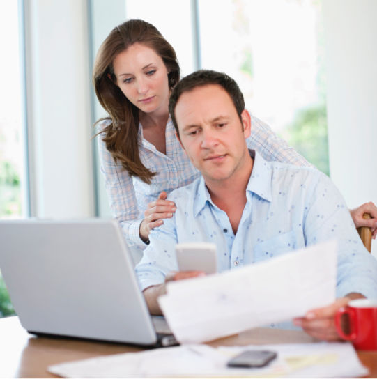 Woman standing looking over a man’s shoulder. Man is seated and looking at a smartphone. Identity theft coverage