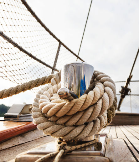 A thick tan rope wrapped around a silver bitt on the wooden deck of a sailboat