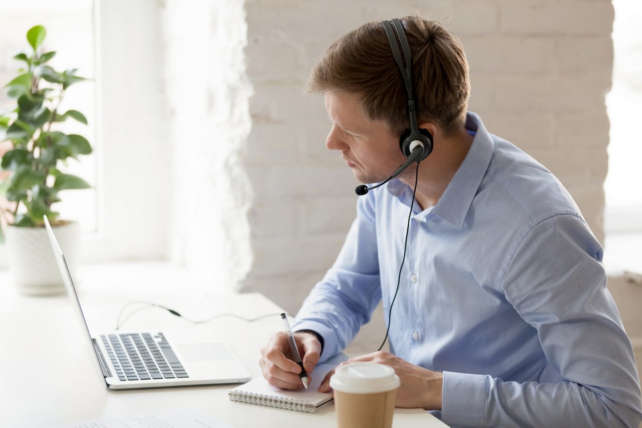 Businessman sitting at workplace improve knowledge use online lessons. Customer service operator wear headset listen client make notes solve problem distantly. Easy learning modern technology concept