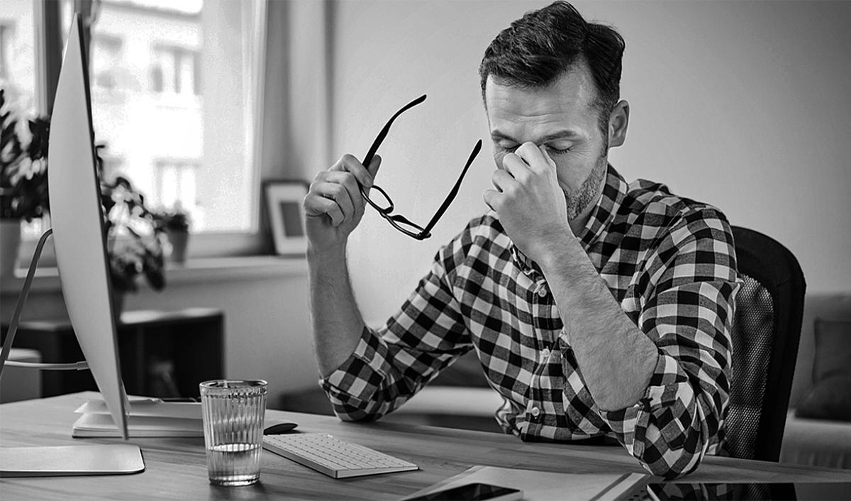 Man rubbing his eyes while sitting at a desk