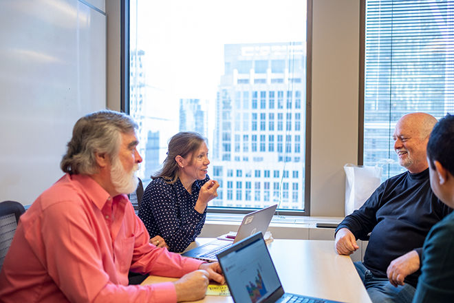 4 coworkers at table with laptops, meeting, smiling, 3 men, 1 woman, older men, beards