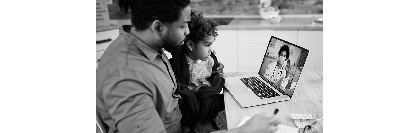 Man holding daughter while looking at laptop