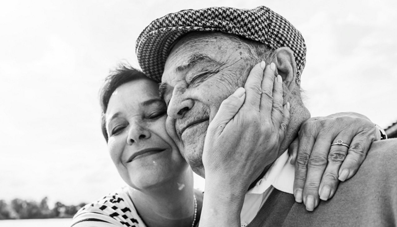 Pareja mayor sonriendo y abrazándose con la mano de ella en la mejilla de él