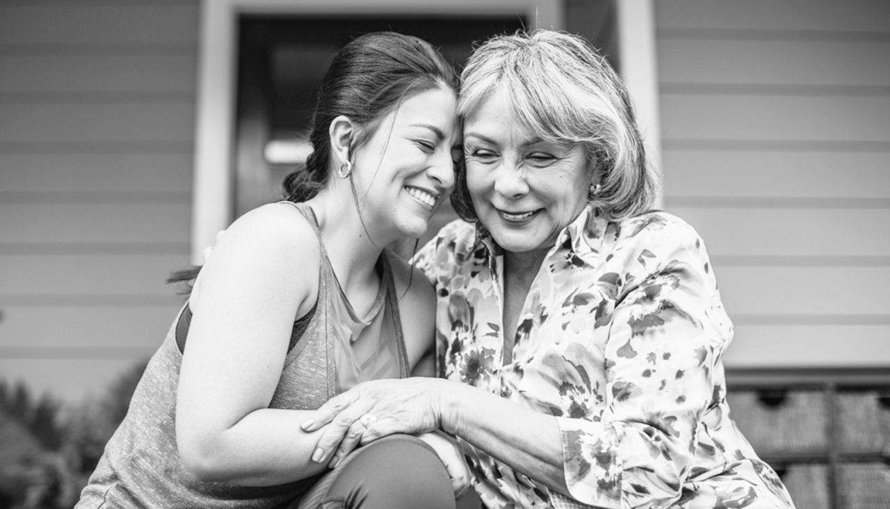 Mother and adult daughter sitting outside while smiling and embracing