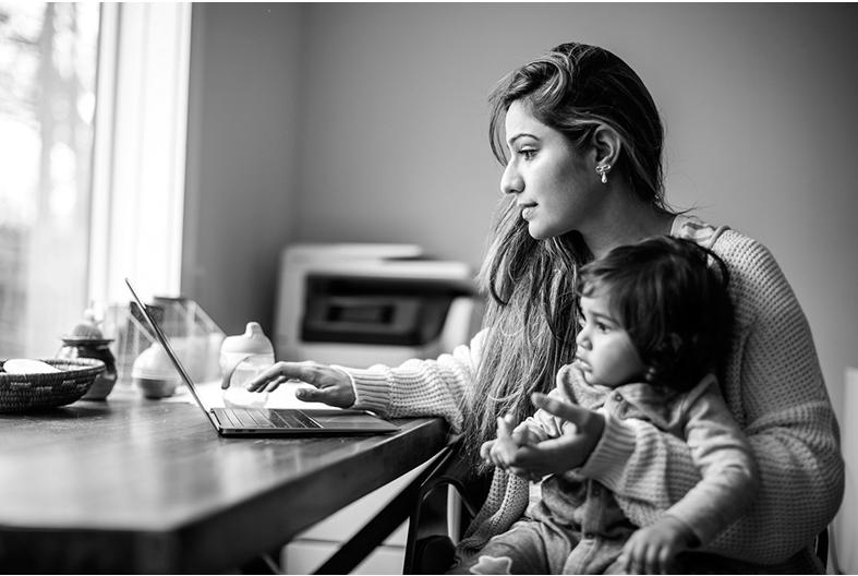 Woman sitting at a table with a computer and a baby in her lap