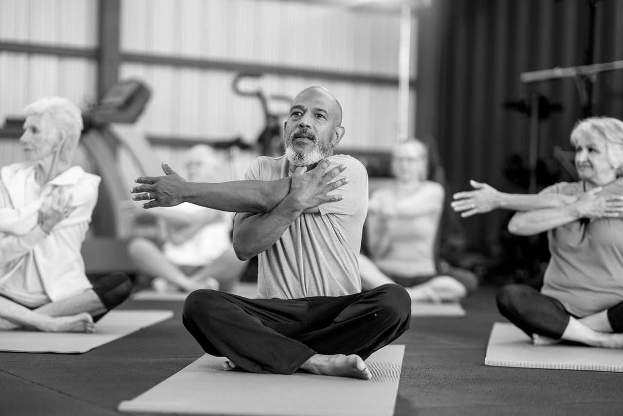 Sitting man stretching his arm, facing us in a class with women behind