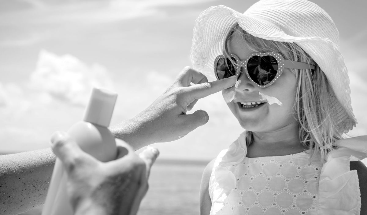 Young girl putting on sunscreen while wearing sunglasses and a hat