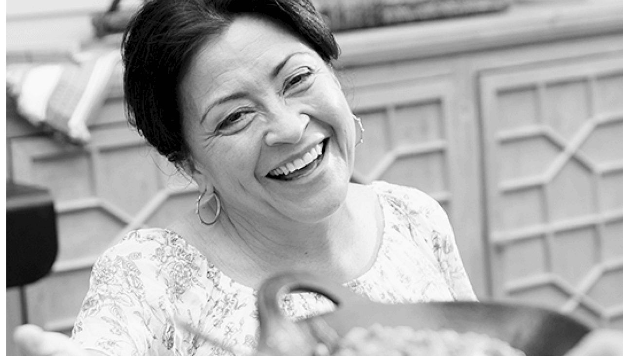 Mujer mayor sonriente mientras le pasan un plato de comida