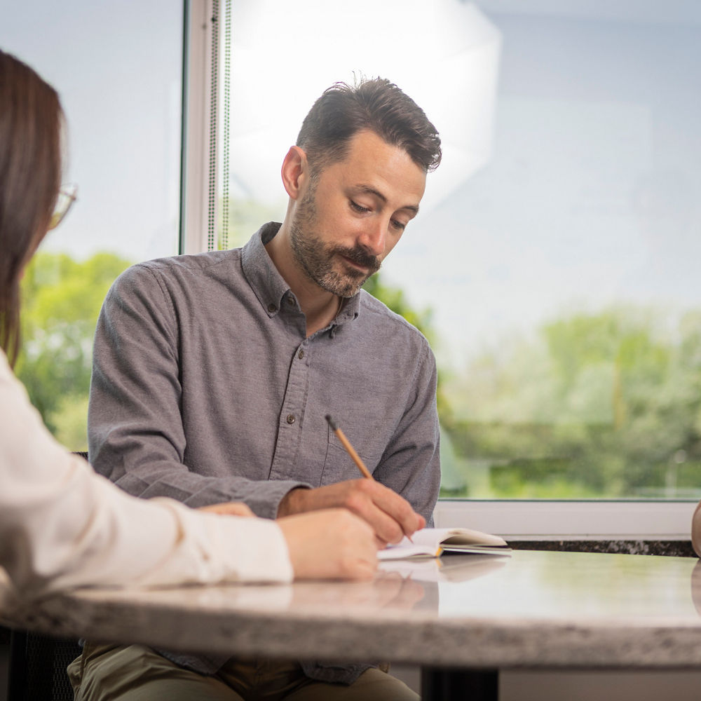 A man writing on paper with his smiling colleagues at a table.