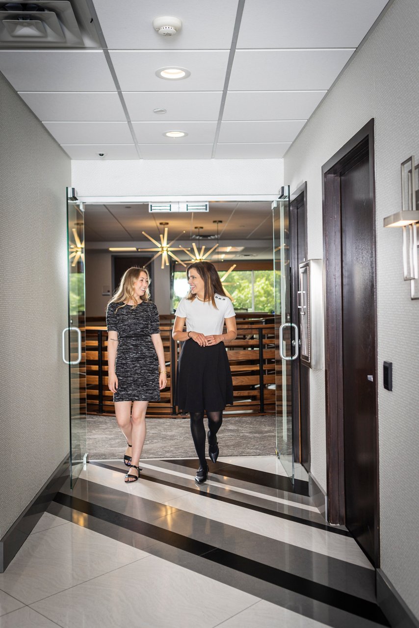 Two women smiling and walking together down a hallway.