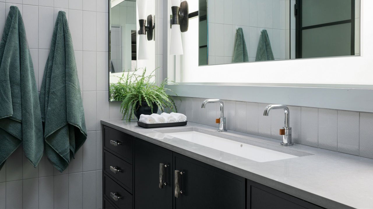 现代卫生间黑虚伪加灰石英反顶机、双槽反射镜和两件绿色长袍挂在灰砖墙上