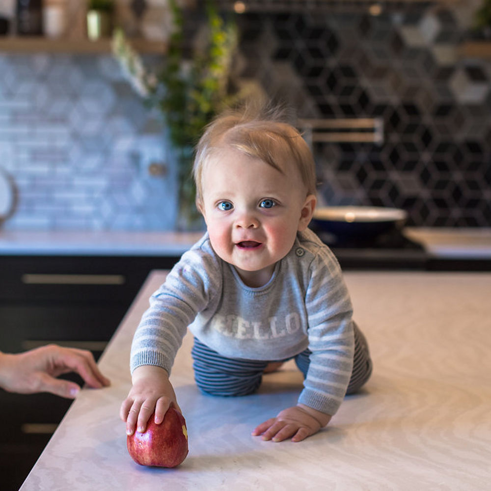 A toddler holding an apple crawls on top of a Cambria Delgatie Matte quartz countertop.