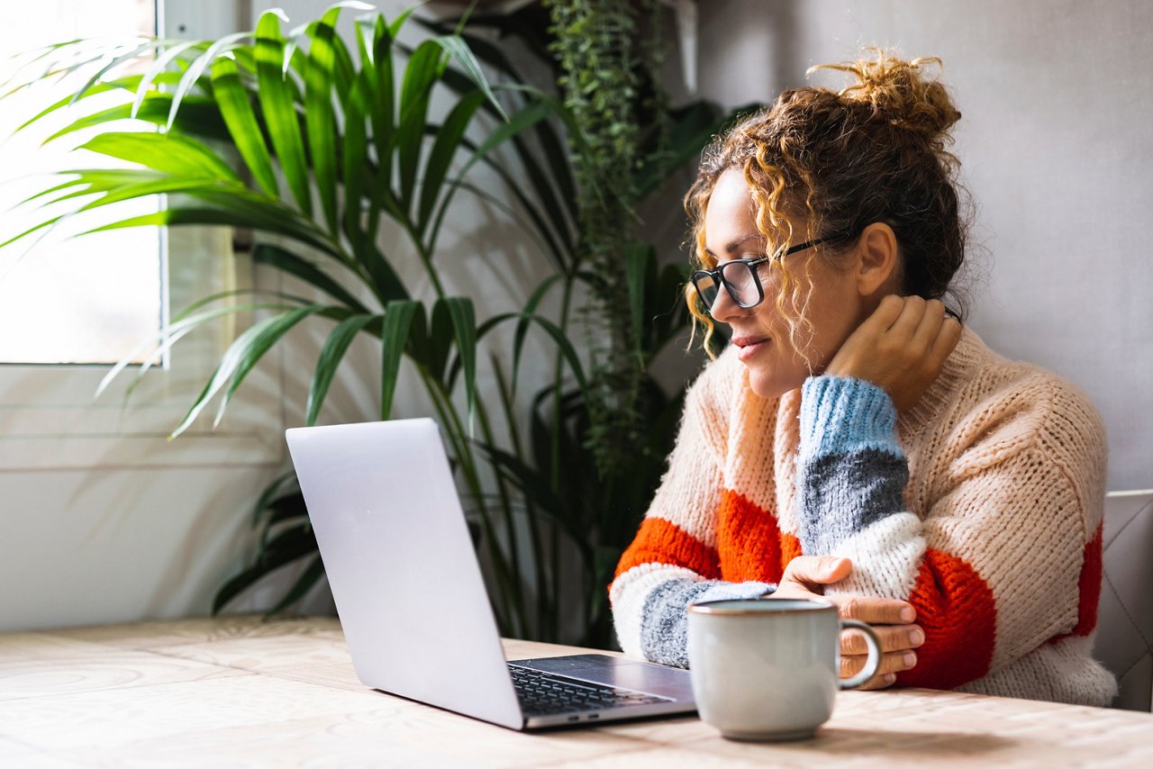 Serene young mature woman looking and reading on laptop online notification email. Pretty female people using computer at home relaxing sitting at the table alone. Modern indoor leisure activity web