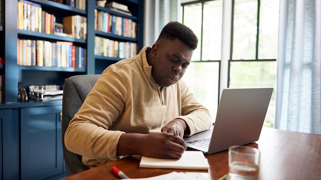 person writing on notebook next to laptop